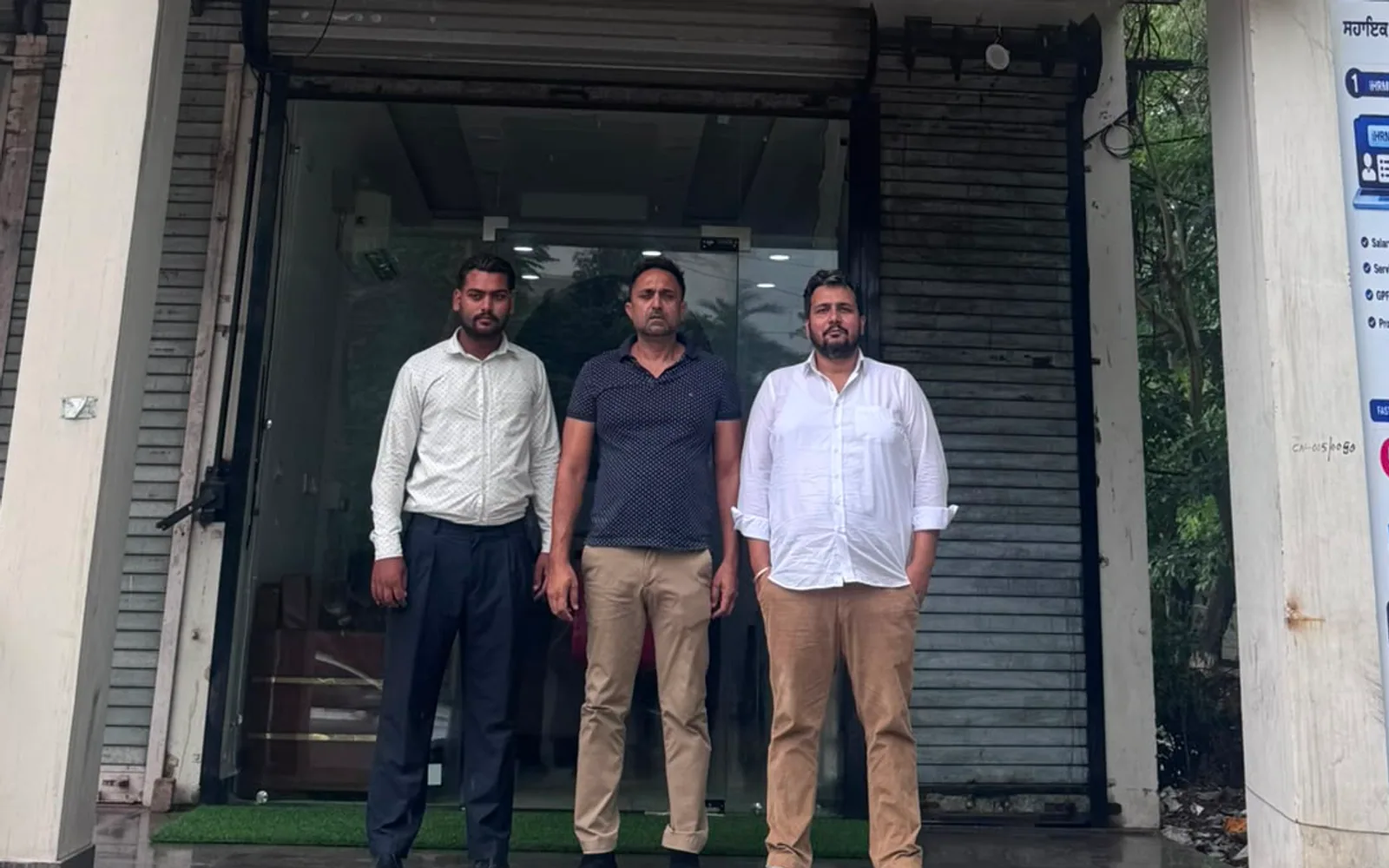 Three men standing outside the glass front of the ground-floor Lifeset Overseas office on Nabha Road, Patiala